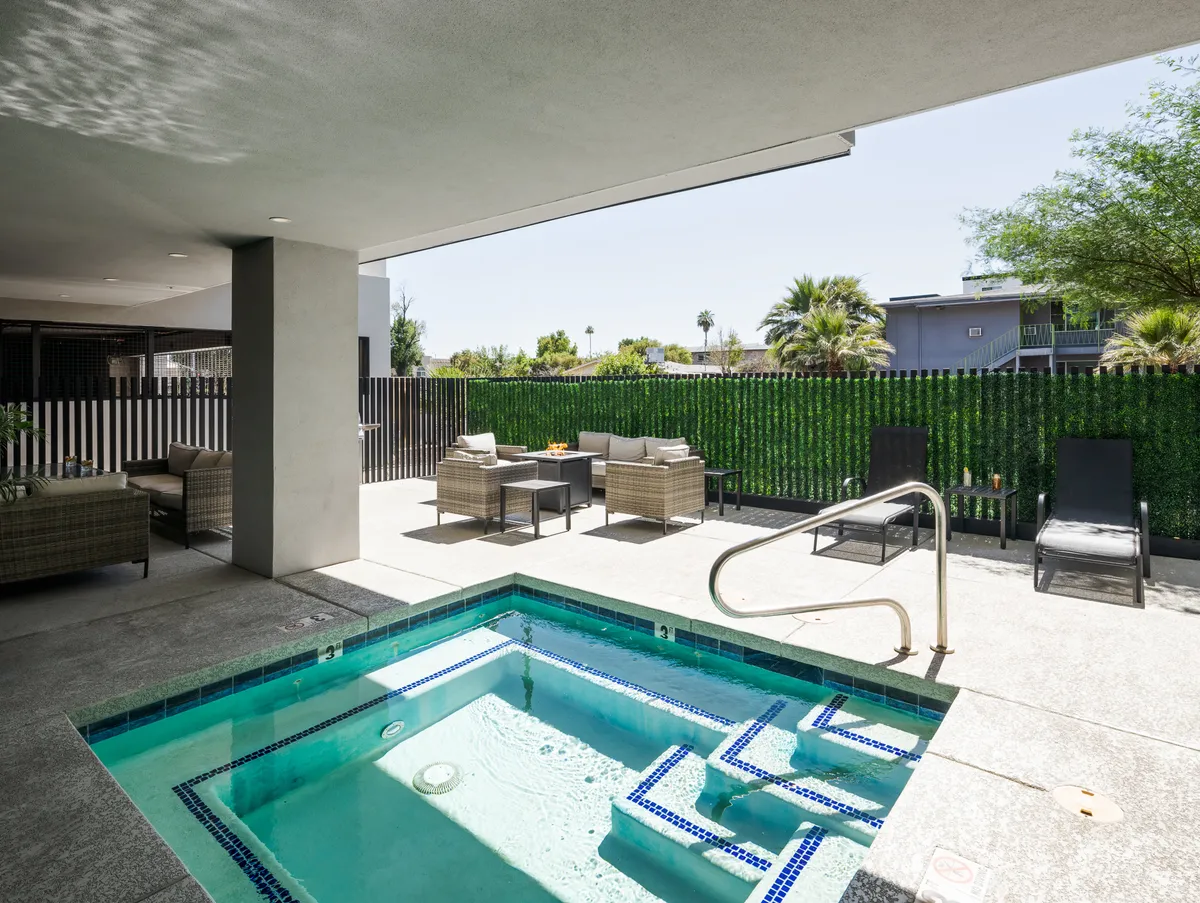 An inviting outdoor hot tub area framed by lush greenery and a stylish fence. A spa pool and comfortable seating encourage relaxation, with space for socializing or unwinding alone. The scene is tranquil, capturing the warmth of Arizona sunsets.