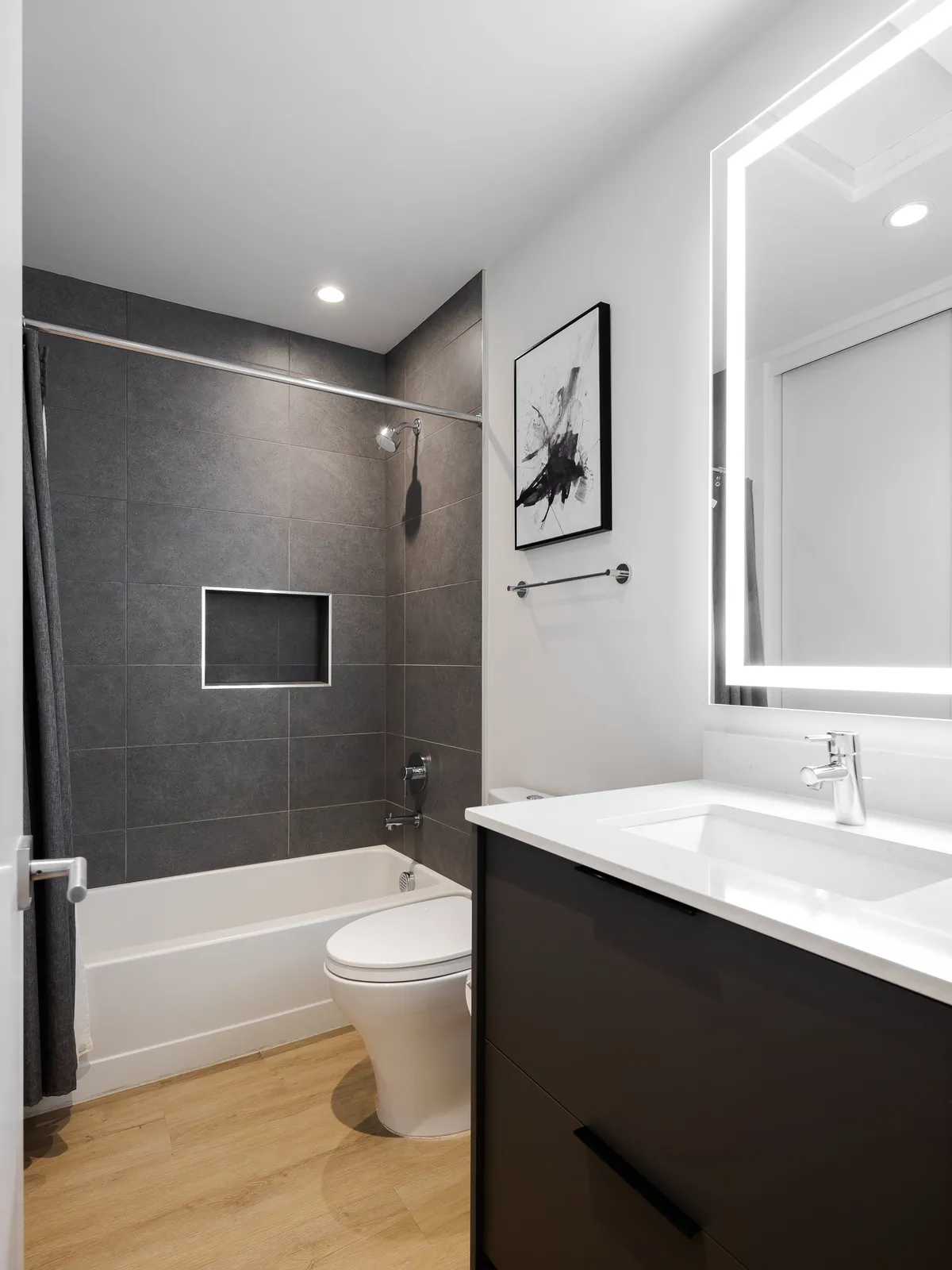 A modern, serene bathroom featuring a bathtub, vanity with a sink, framed artwork, and a backlit mirror. The space feels inviting and well-appointed, designed for soothing self-care routines or a relaxing soak after a busy day.