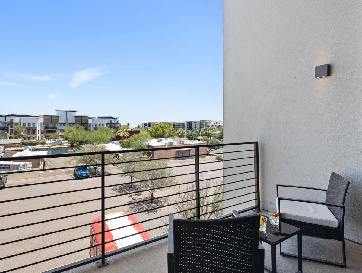An inviting private balcony with cozy seating, potted plants, and a panoramic city view. The tranquil mood suggests a versatile space for morning coffee or evening conversations, extending the interior’s social atmosphere outdoors.