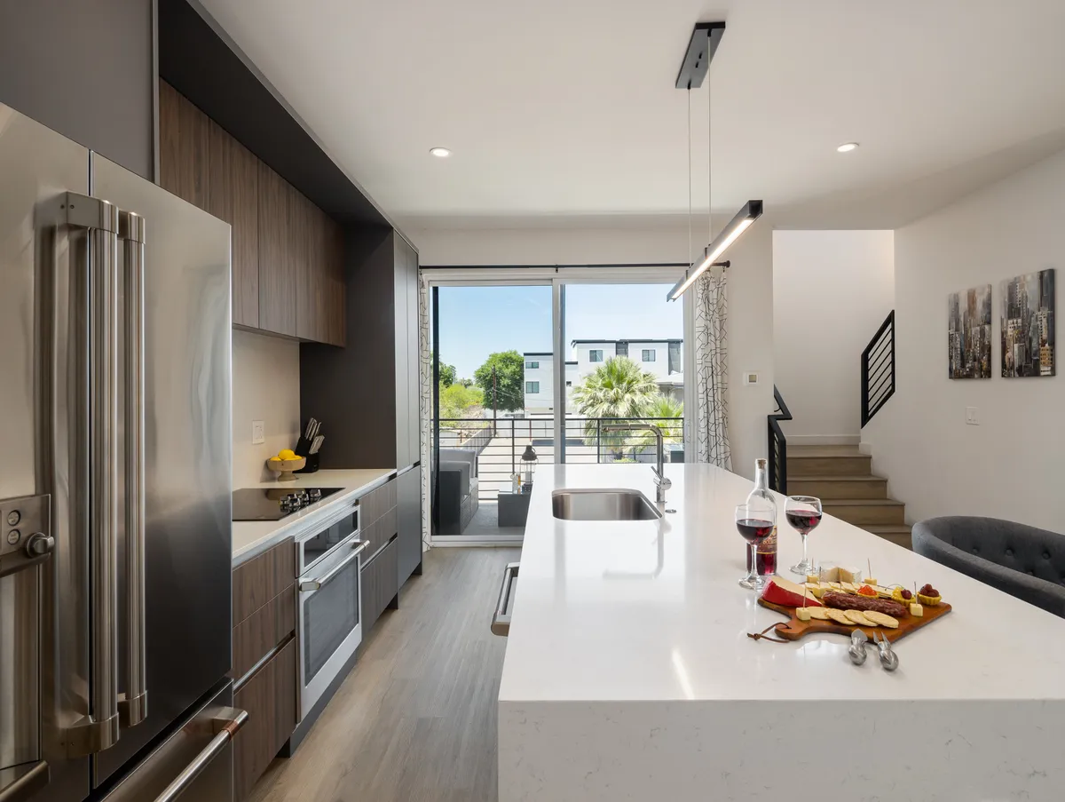A sleek, modern kitchen centered around a large island with bar seating, framed by expansive windows offering outdoor views. A charcuterie board and wine set the scene for entertaining, and the overall layout supports casual dining or festive gatherings.