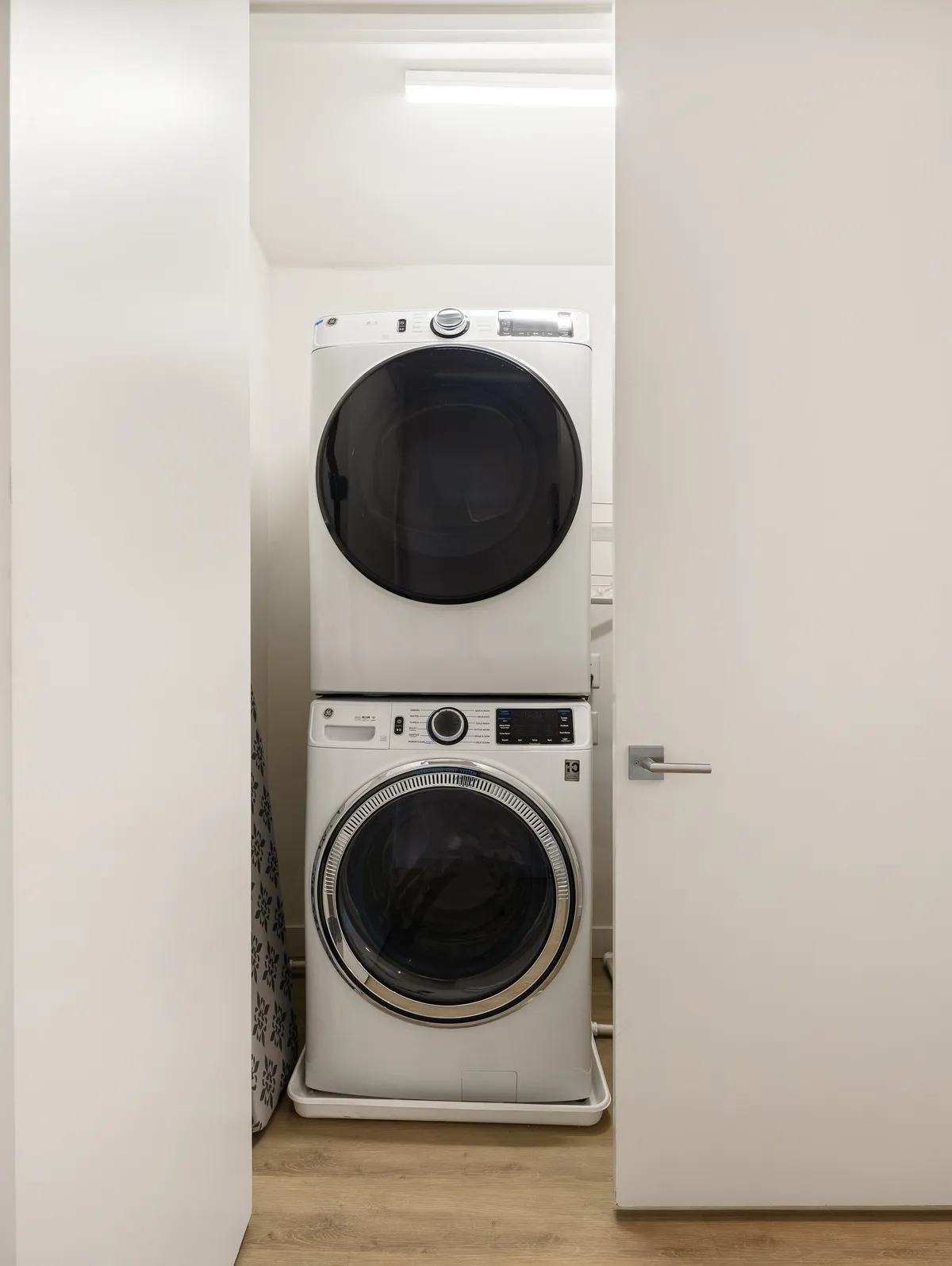A bright and efficient laundry area with a stacked washer and dryer, minimalist cabinetry, and ample lighting, offering a practical solution for everyday needs within the unit.