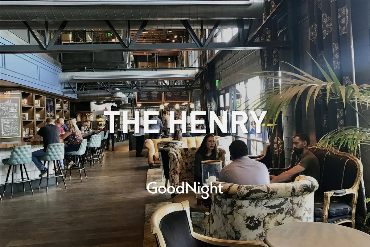 A lively, modern open-concept living and bar area featuring ample seating, decorative plants, and large windows that let in natural light. People are enjoying drinks and meals together, creating a relaxed yet social atmosphere perfect for gatherings.