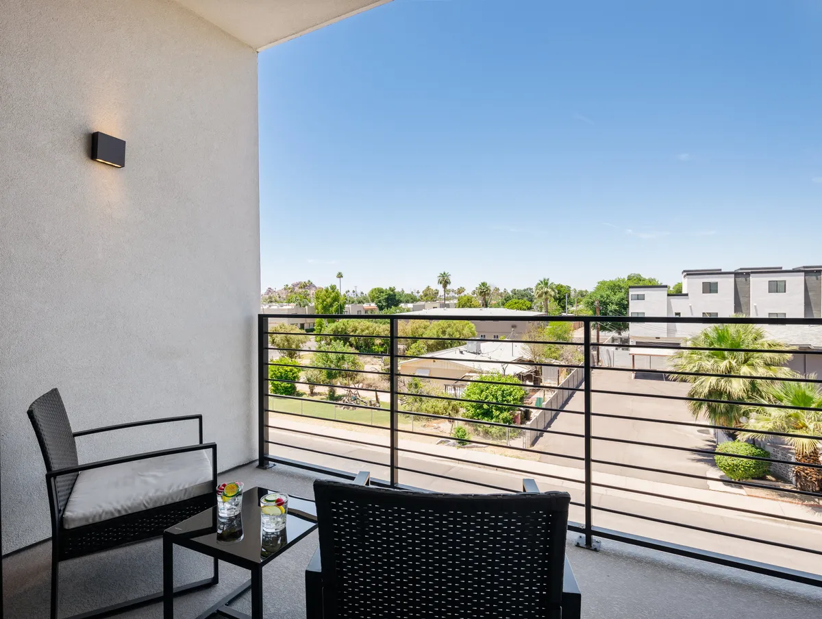A tranquil balcony seating area overlooks lush greenery, with decorative drinks set out on the table. The space feels inviting and ideal for relaxation or small social gatherings, embodying the essence of private outdoor living.