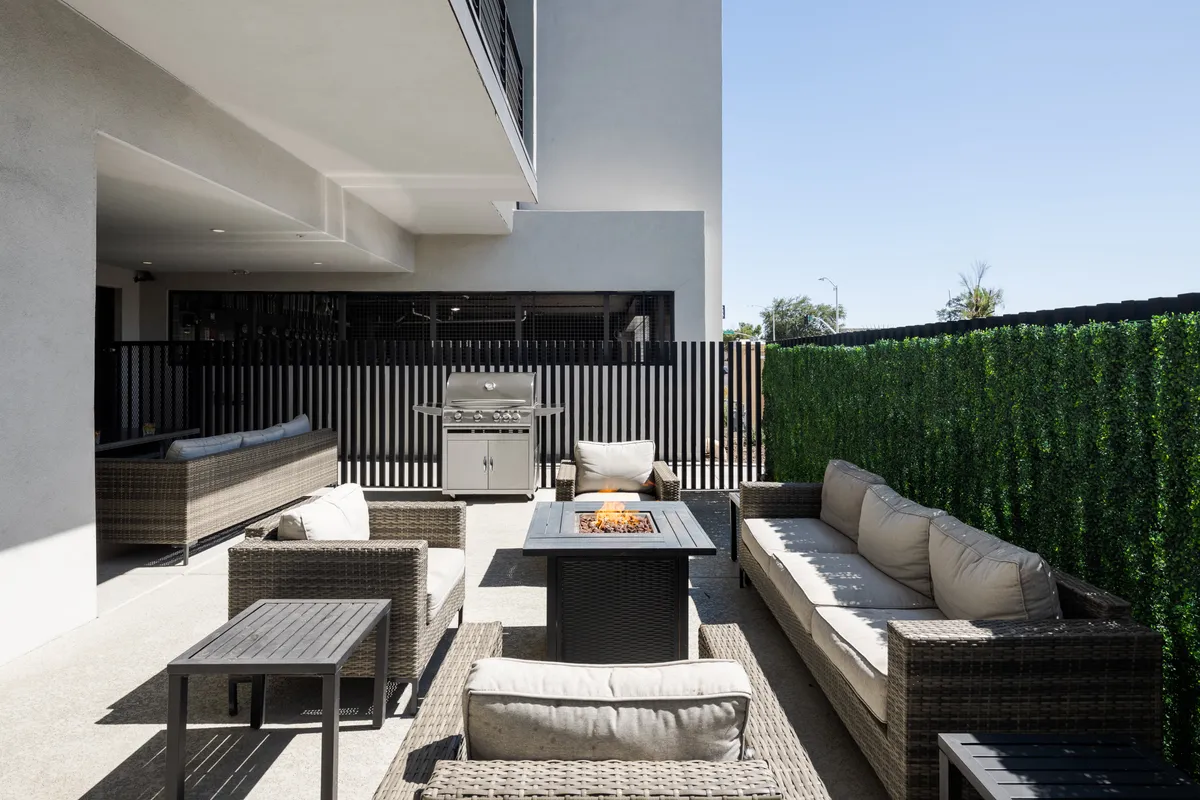 A cozy exterior lounge set around a glowing fire pit, with a BBQ grill and ample seating for outdoor dining. The space is surrounded by greenery, evoking a sense of comfort and togetherness for memorable gatherings under the sky.